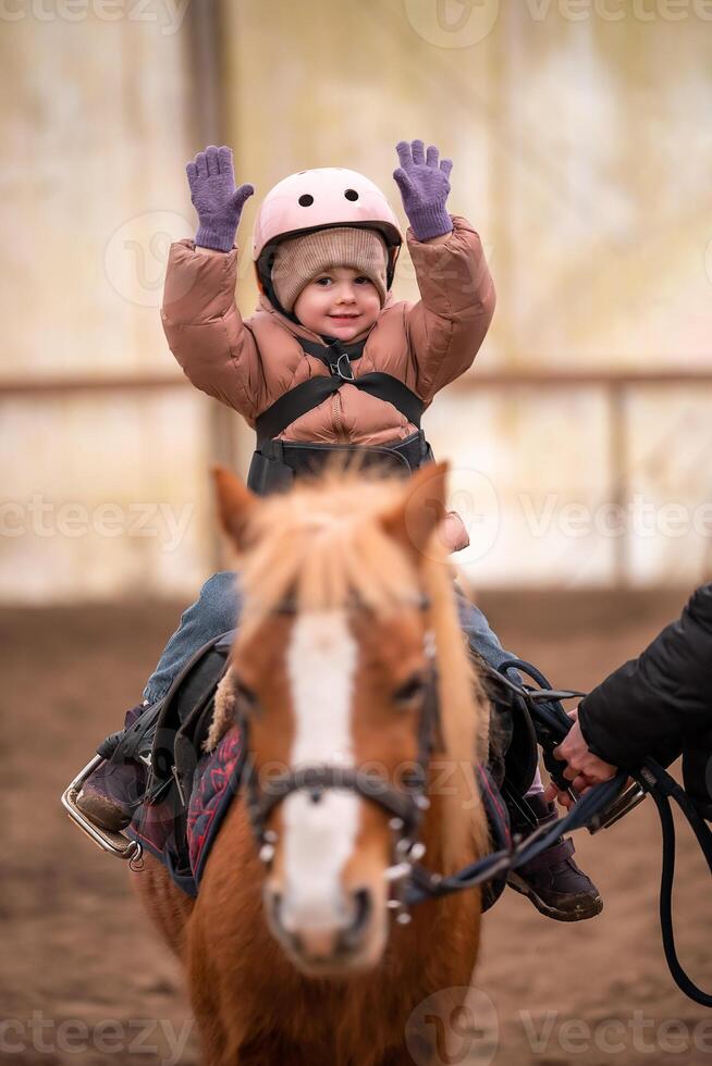 Little Child Riding Lesson. Three-year-old girl rides a pony and does exercises. High quality photo