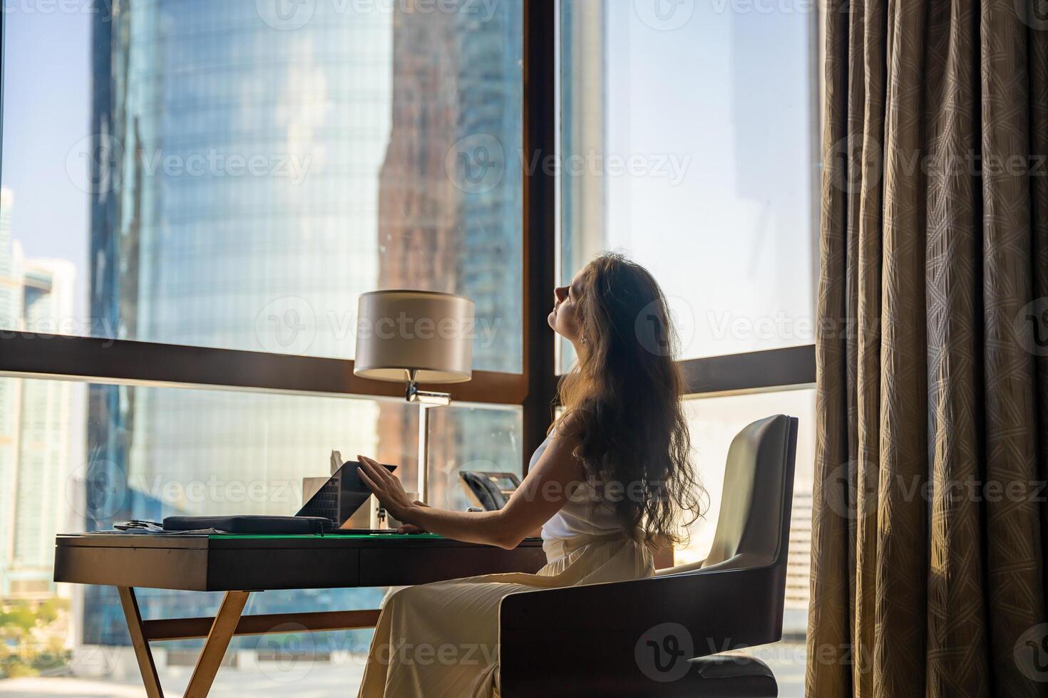 Stylish businesswoman freelancer stops working with laptop, she is sitting on the chair, enjoying panoramic view in window with city background. Low key photo. High quality photo