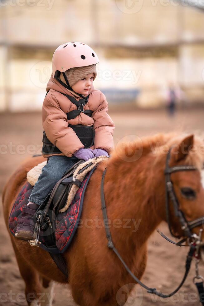 Little Child Riding Lesson. Three-year-old girl rides a pony and does exercises. High quality photo