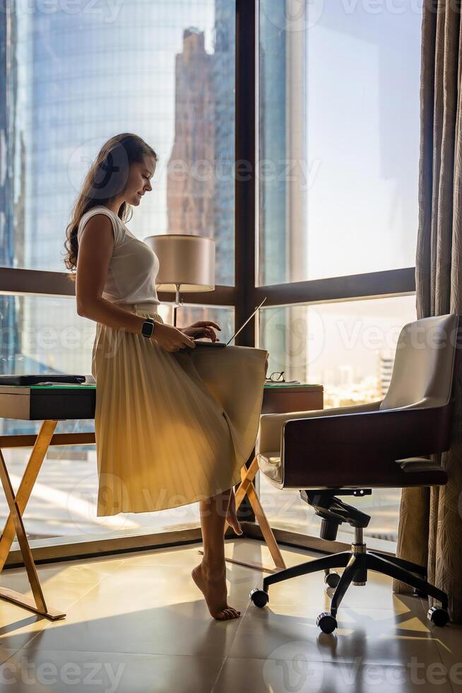 Stylish businesswoman freelancer working with laptop and sitting on the table, enjoying panoramic view in the city background. Low key photo. High quality photo