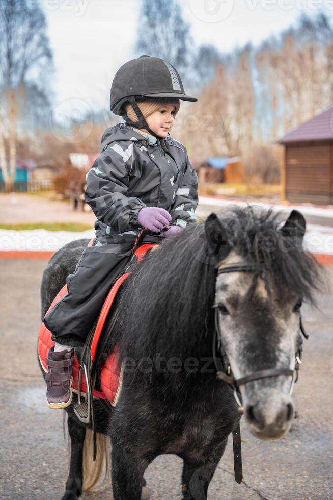 Little cute girl riding a little horse or pony in the winter in field in the winter. High quality photo