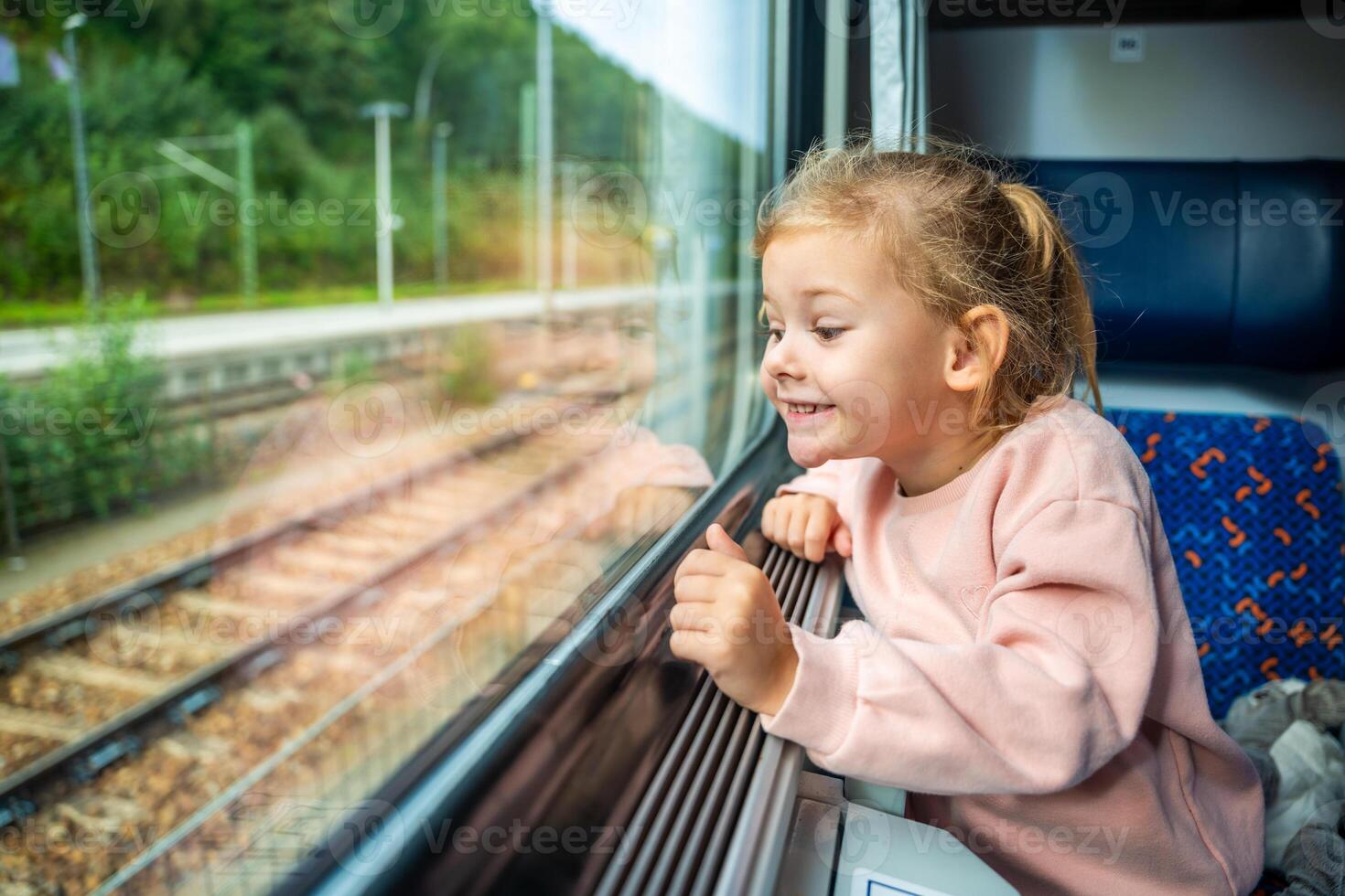 Happy little girl looking out train window outside, while it moving. Traveling by railway, Europe photo