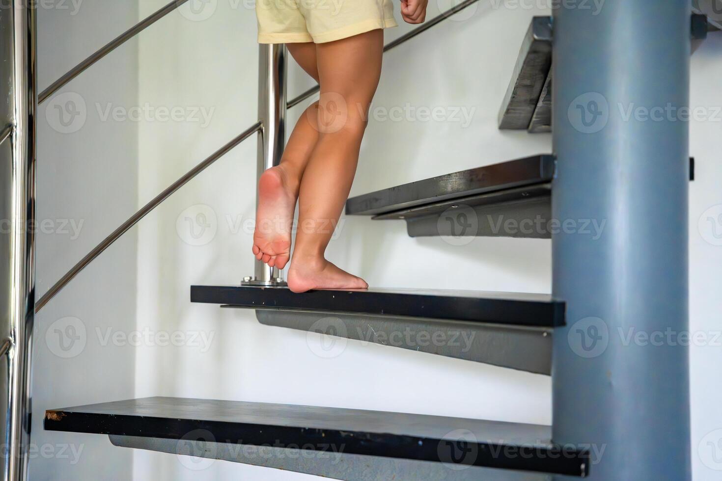 cerca arriba ver de pequeño niño pies yendo arriba el escalera a moderno hogar, niño alpinismo espiral escalera foto