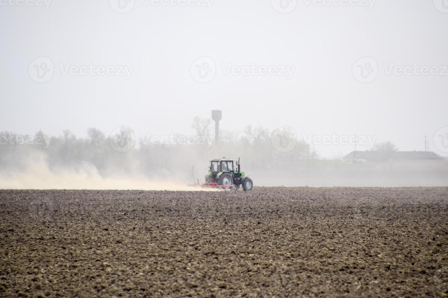 el tractor gradas el suelo en el campo y crea un nube de polvo detrás eso foto