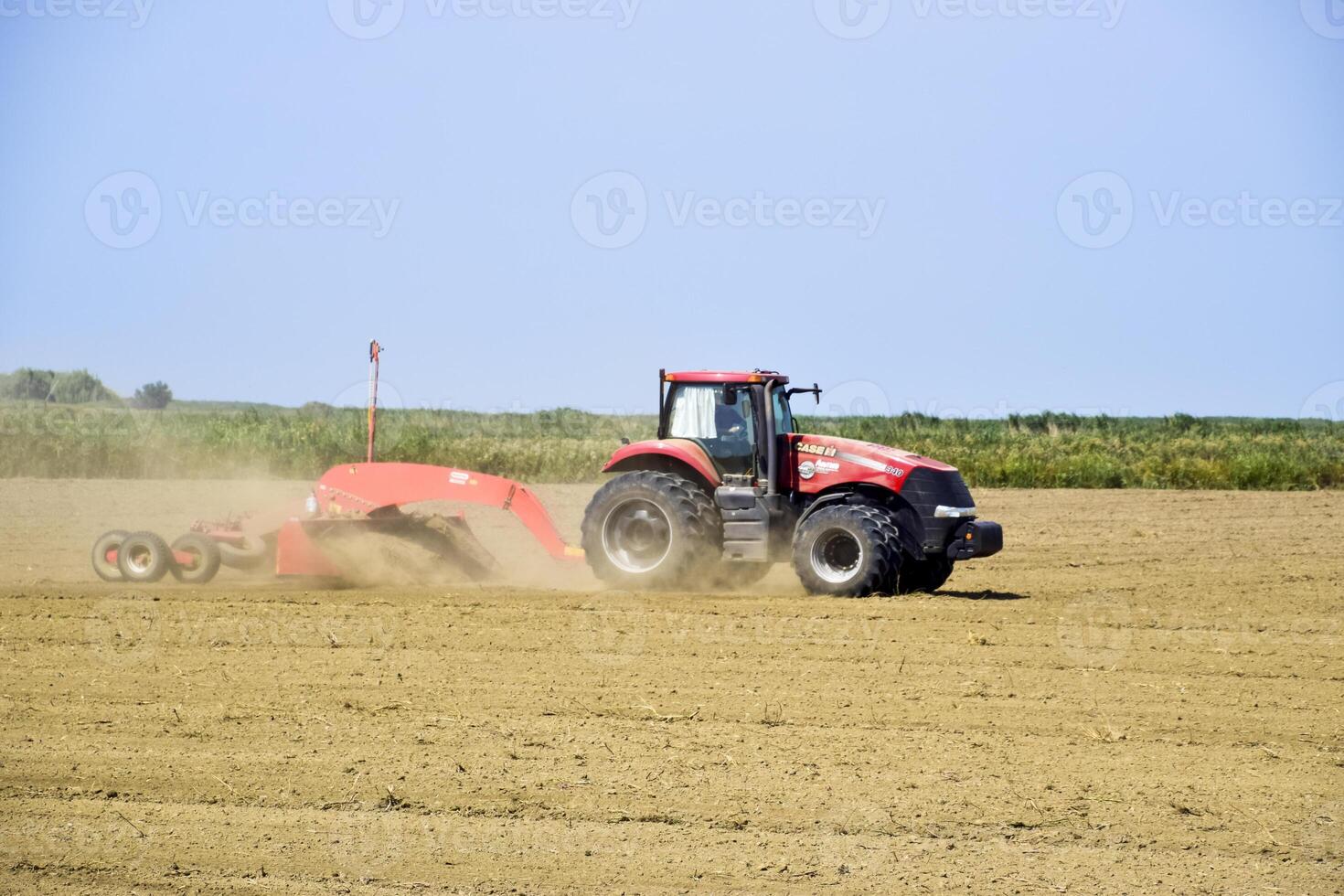 Tractor with a grader aligns the soil on the field. The tractor raised dust. photo