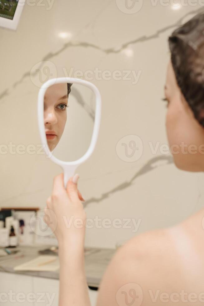 A smiling woman looks in the mirror in the cosmetologist's office. Vertical photo