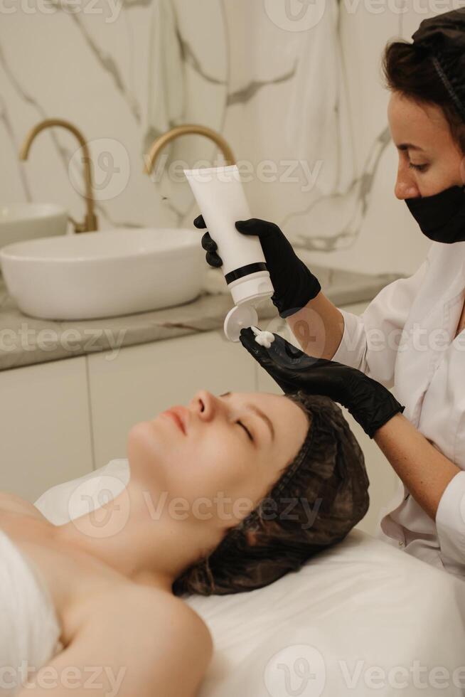 de cerca de el de esteticista manos aplicando crema a el clientela cara y haciendo un masaje. facial piel cuidado. vertical foto