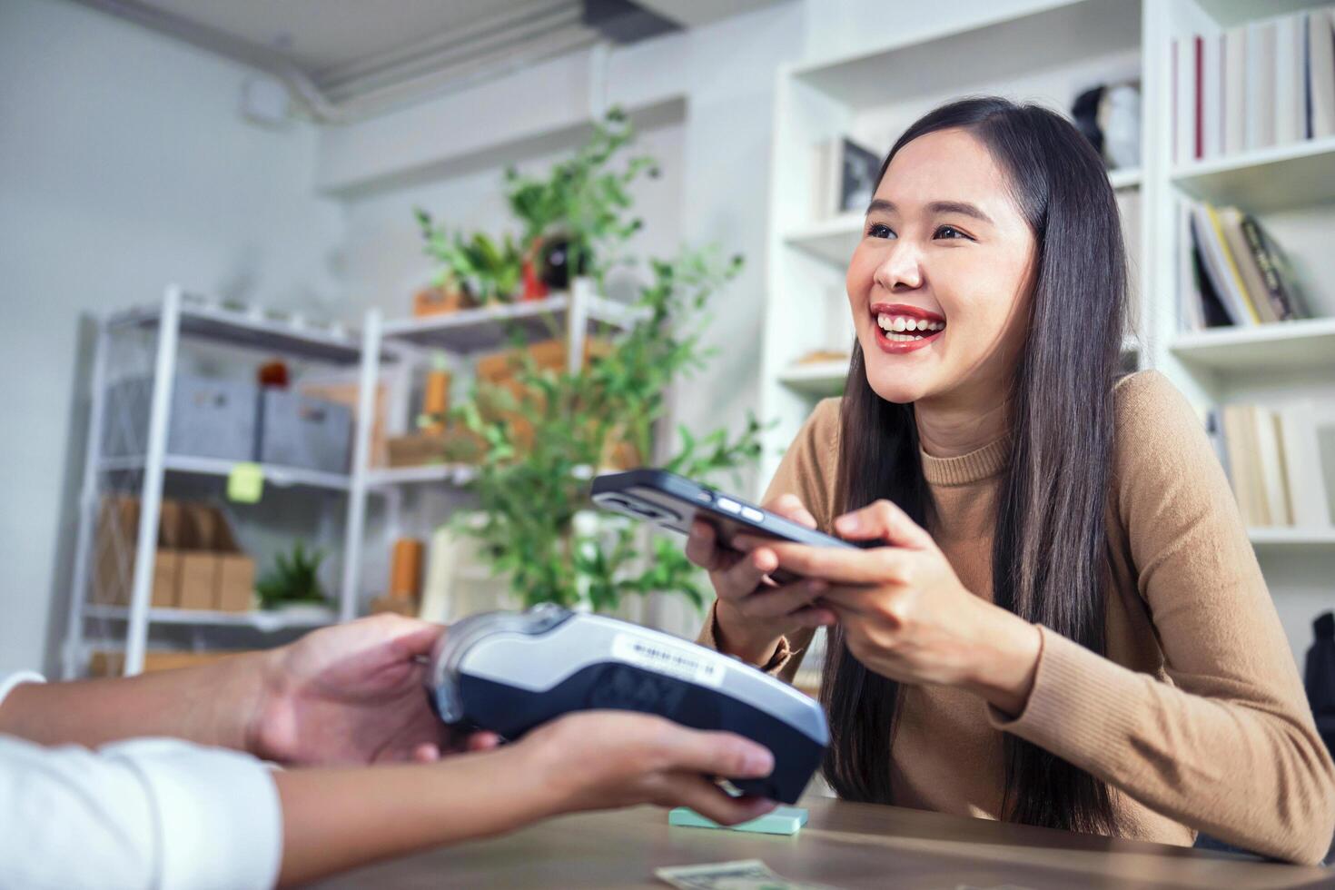 Young Asian woman smiling and paying with smartphone in restaurant photo