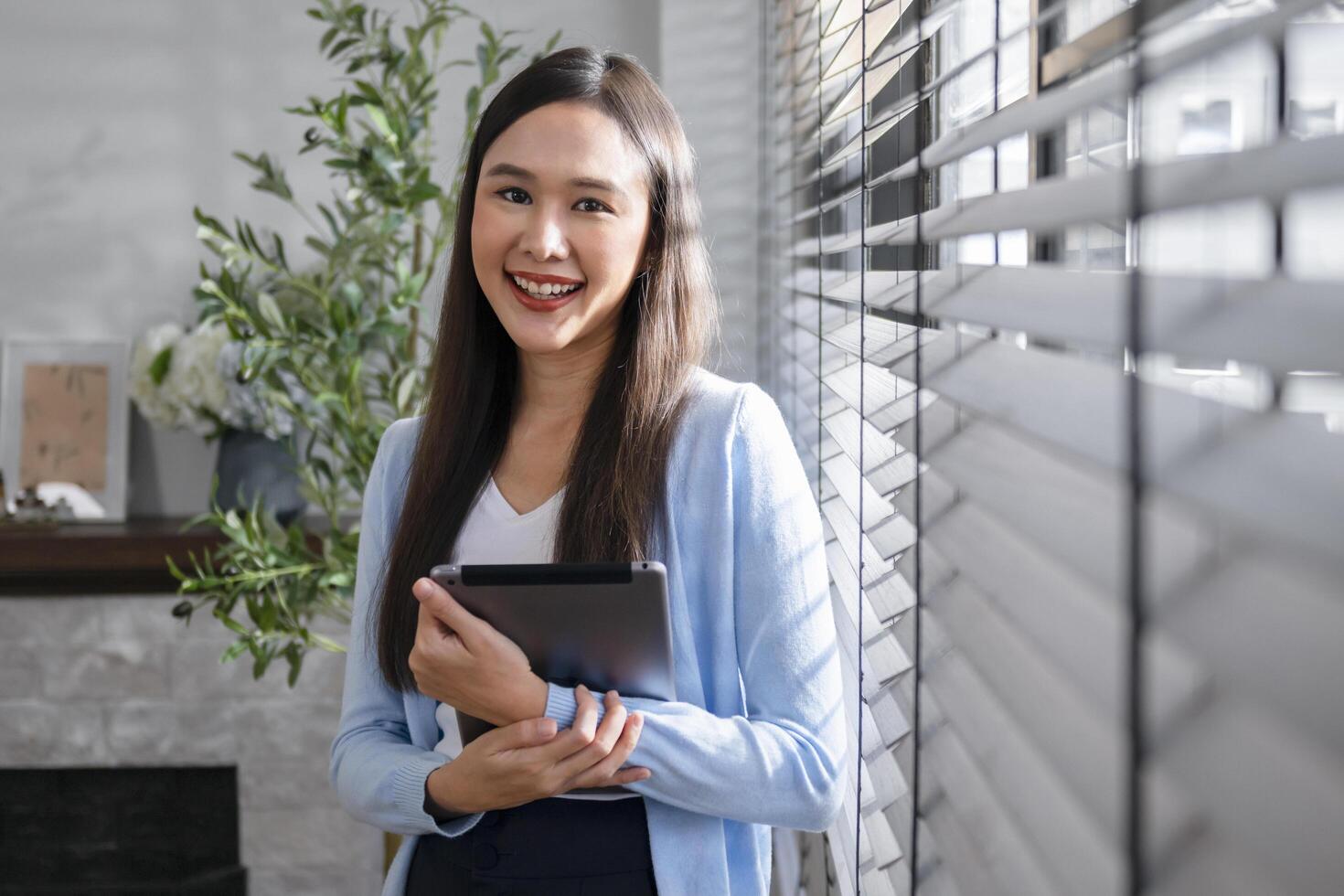 Confident businesswoman standing smiling holding iPad in office photo