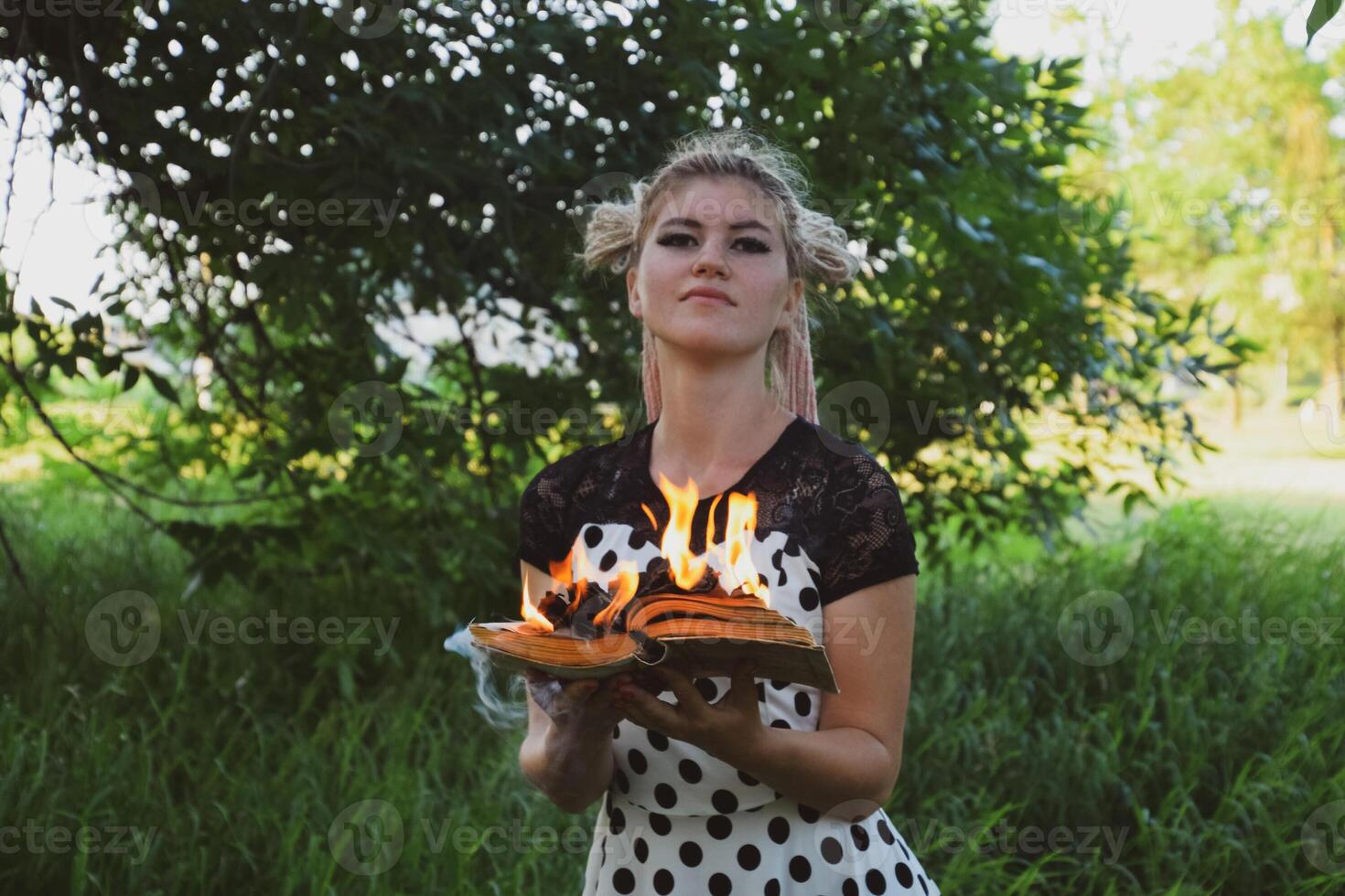 niña sostiene un ardiente libro en su manos. un joven mujer en un bosque quemaduras un libro. foto