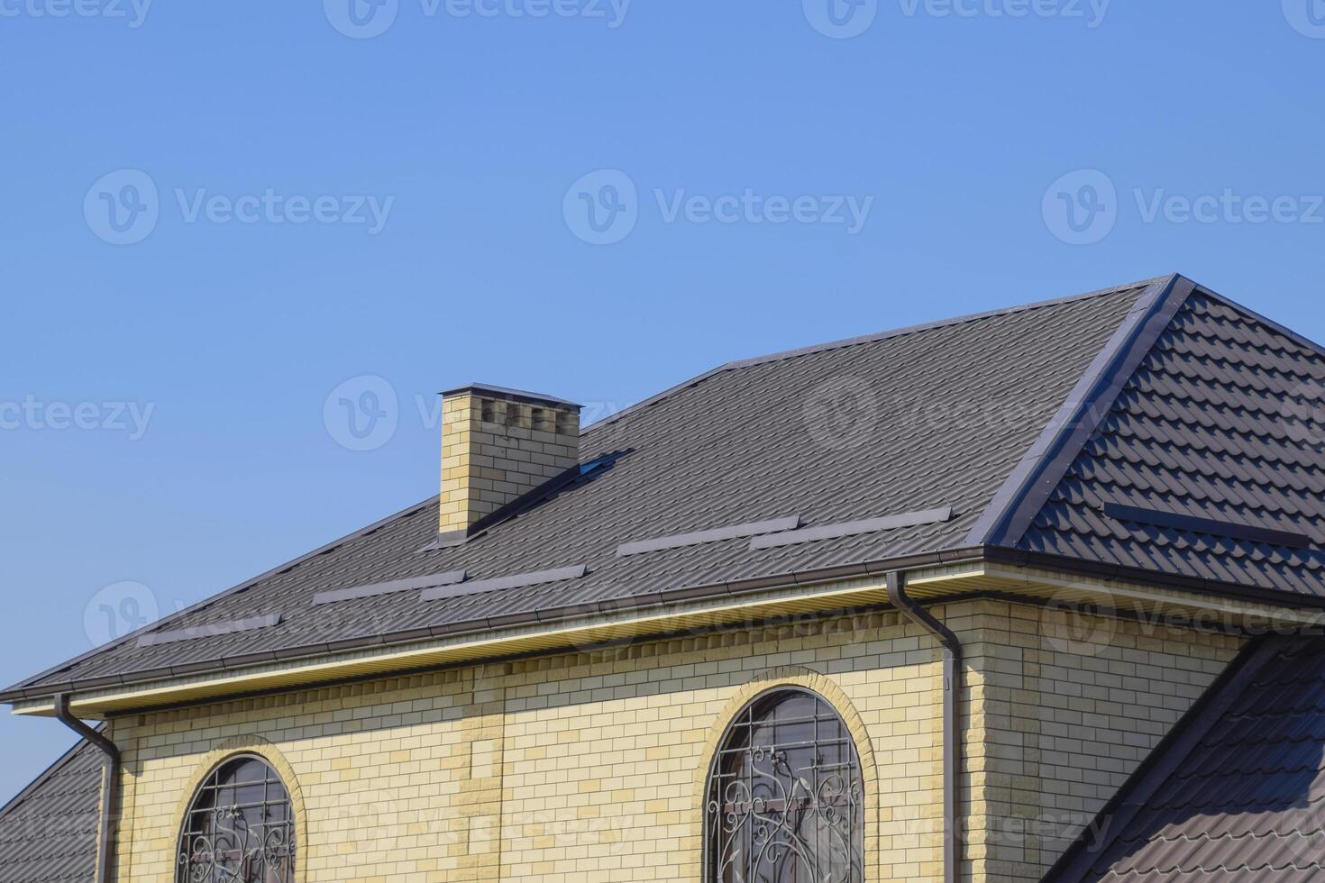 House of yellow brick and brown corrugated roof made of metal. Lattices on the windows. photo