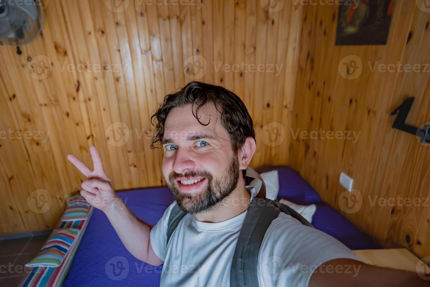 Tourist boy taking a selfie inside a rental room. He makes the peace sign with his hands. photo