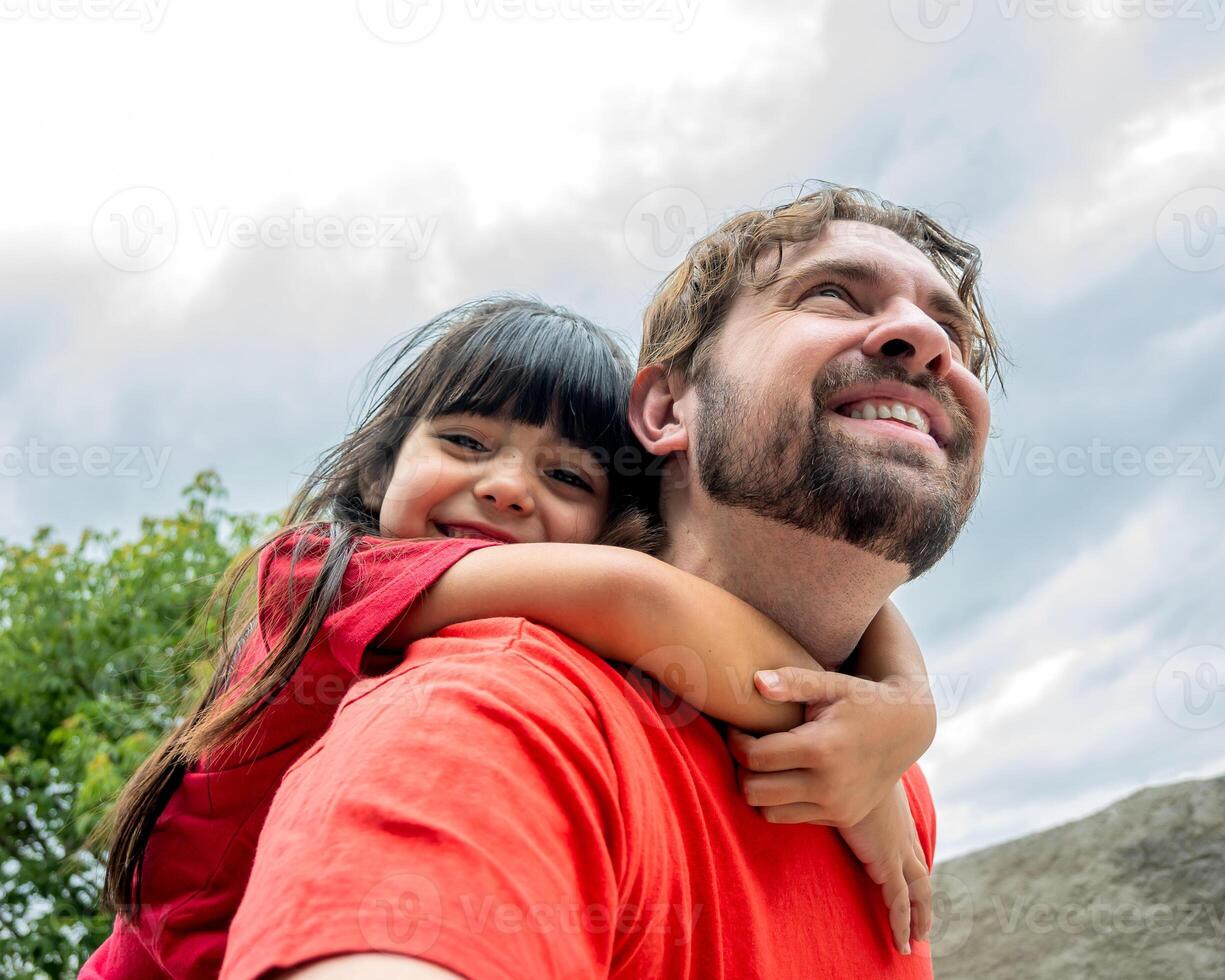 Latina daughter and father. Her father gives her a piggyback and her looking at camera. photo