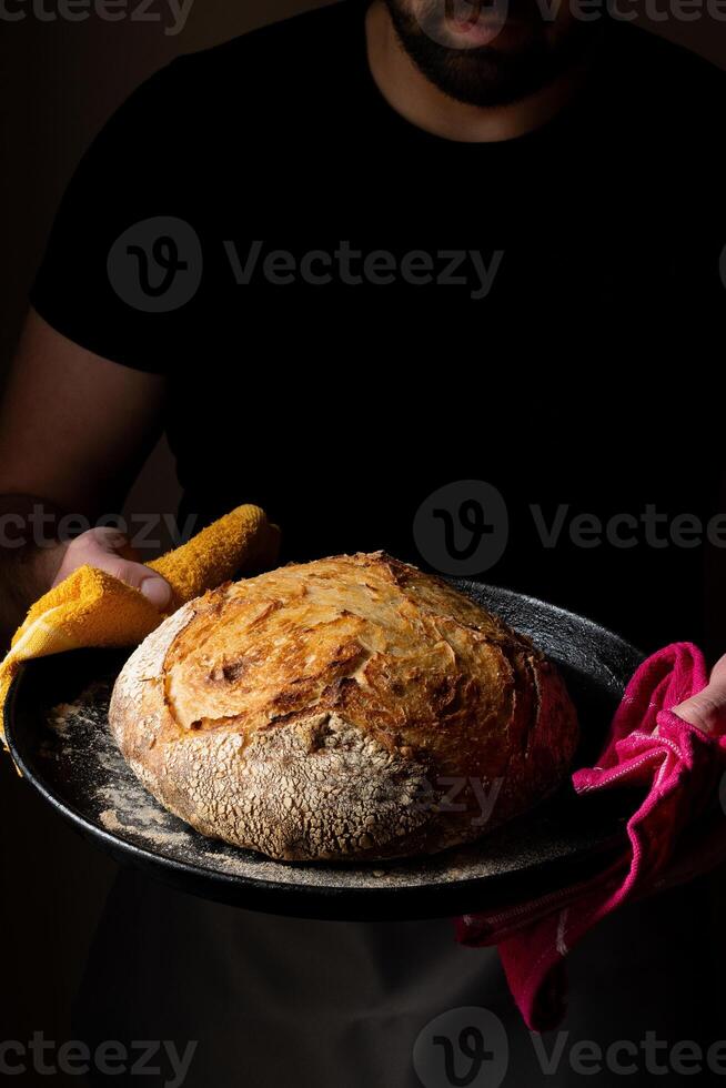 atractivo joven caucásico cocinero posando con blanco de masa fermentada un pan. foto