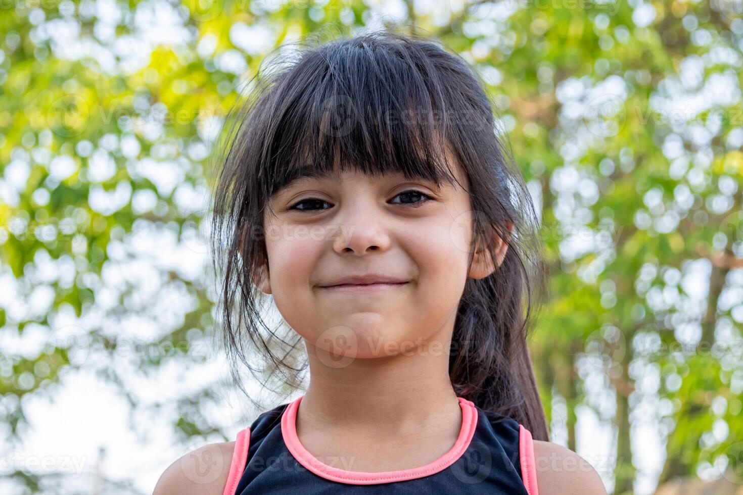 de cerca retrato de su. ella es amigable, encantador, dulce, curioso y alegre. pequeño niña al aire libre en Deportes ropa. foto