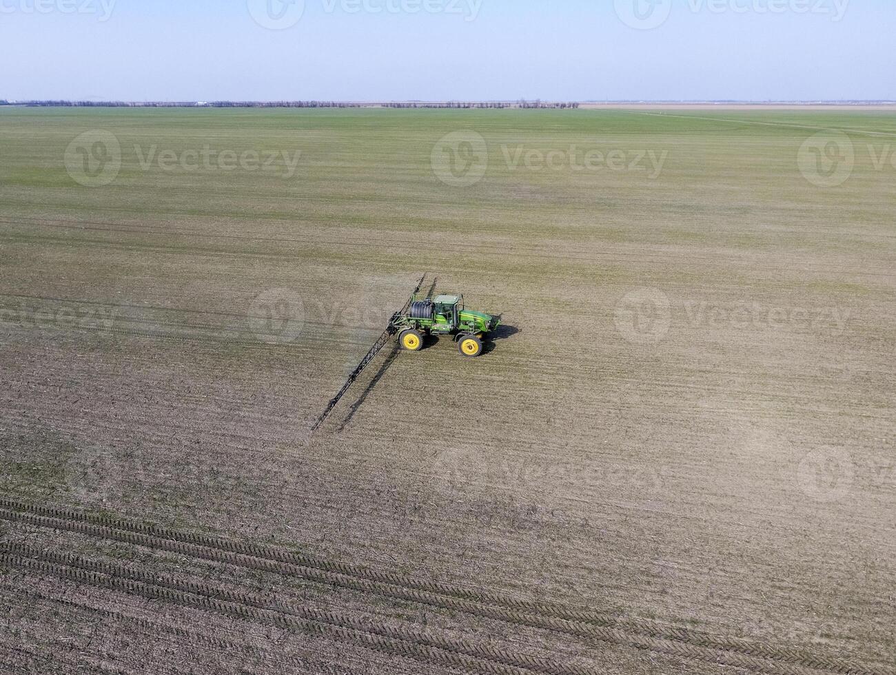 Tractor with hinged system of spraying pesticides. Fertilizing with a tractor, in the form of an aerosol, on the field of winter wheat. photo