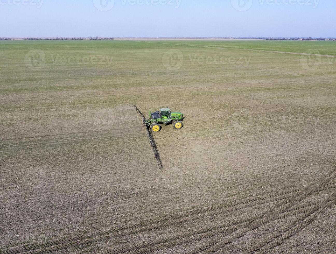 Tractor with hinged system of spraying pesticides. Fertilizing with a tractor, in the form of an aerosol, on the field of winter wheat. photo
