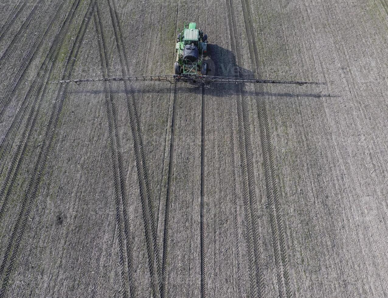 Tractor with hinged system of spraying pesticides. Fertilizing with a tractor, in the form of an aerosol, on the field of winter wheat. photo