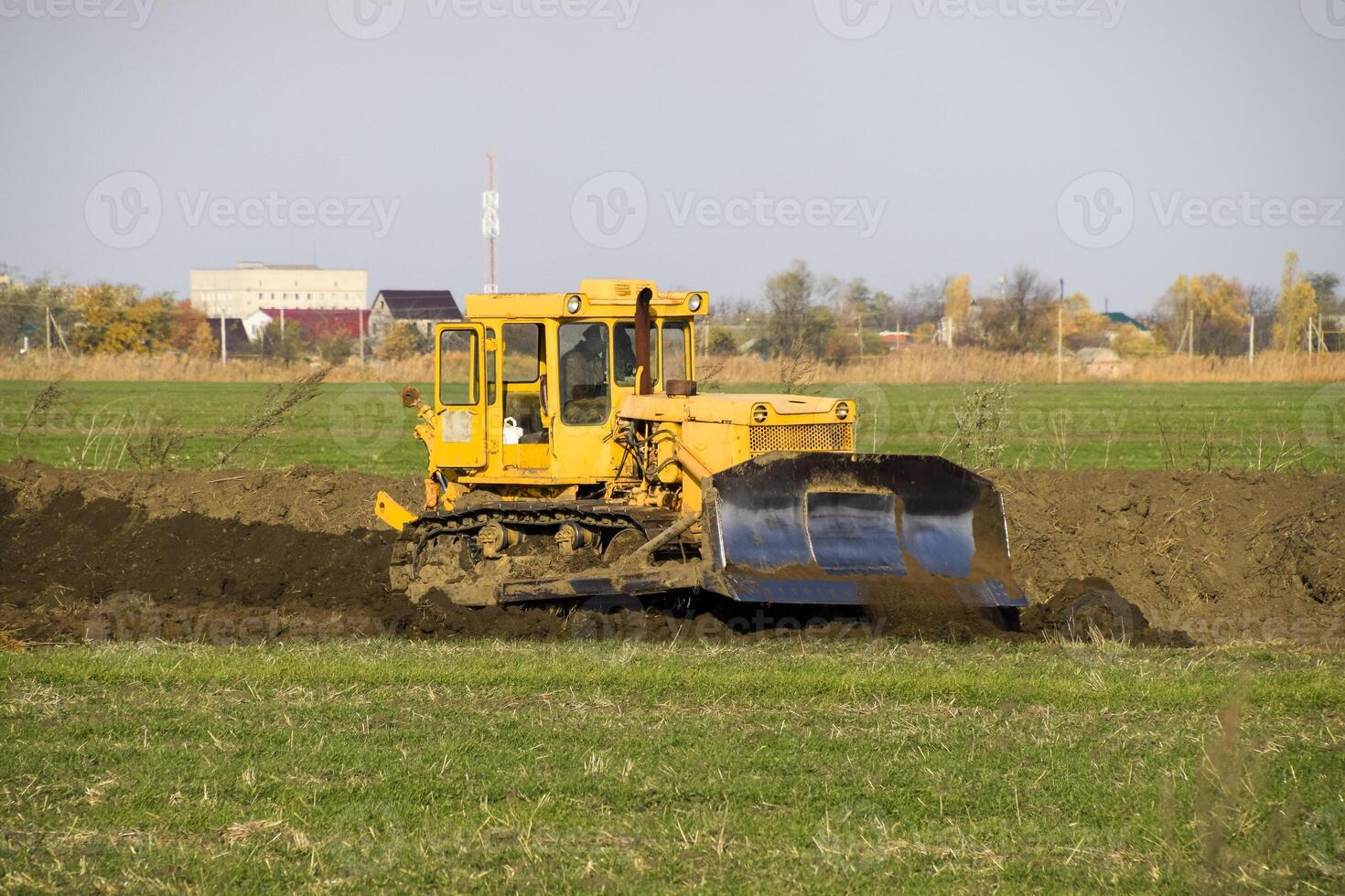 The yellow tractor with attached grederom makes ground leveling. photo