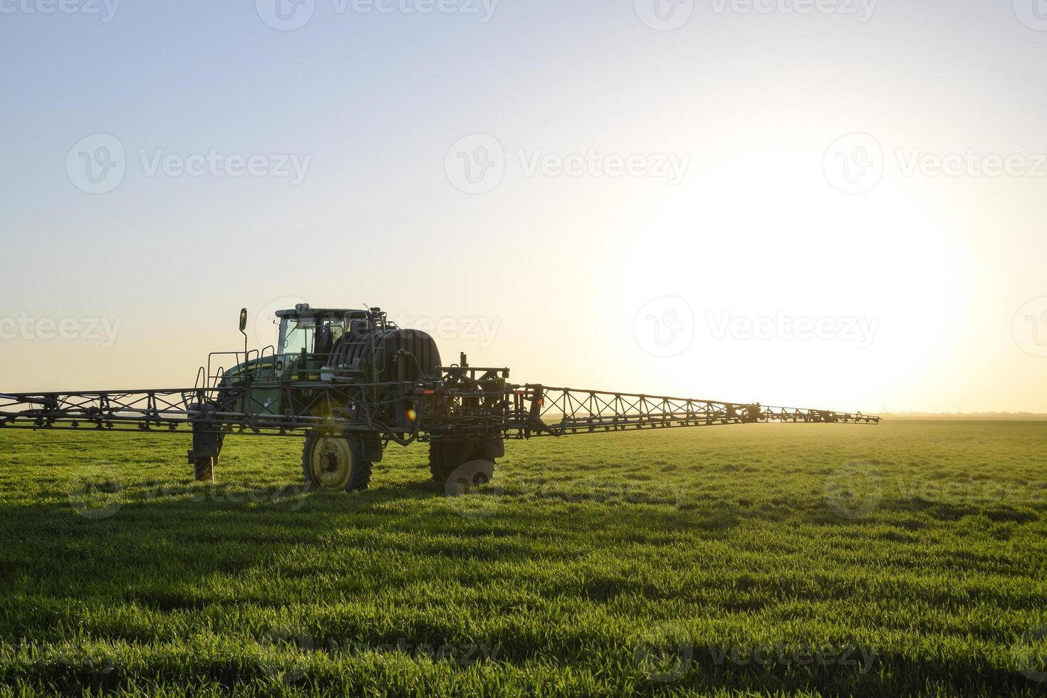 Tractor on the sunset background. Tractor with high wheels is making fertilizer on young wheat. The use of finely dispersed spray chemicals photo