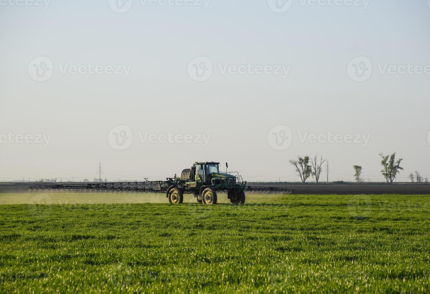 Tractor on the sunset background. Tractor with high wheels is making fertilizer on young wheat. The use of finely dispersed spray chemicals photo