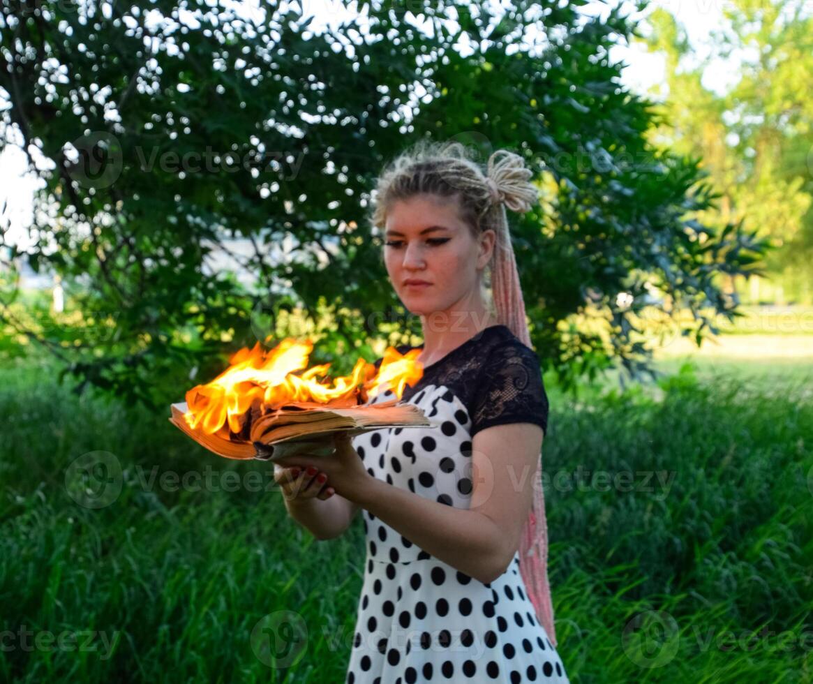 niña sostiene un ardiente libro en su manos. un joven mujer en un bosque quemaduras un libro. foto