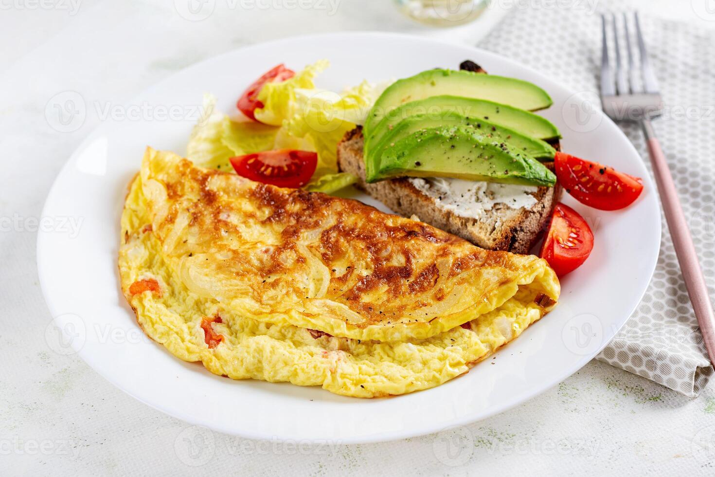 Omelette with tomatoes and toast with avocado on white plate.  Frittata - italian omelet. photo