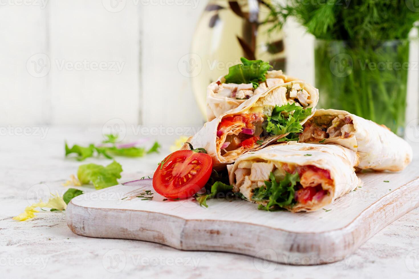 Grilled tortilla wraps with chicken and fresh vegetables on white wooden board. Chicken burrito. Mexican food. Healthy food concept. photo