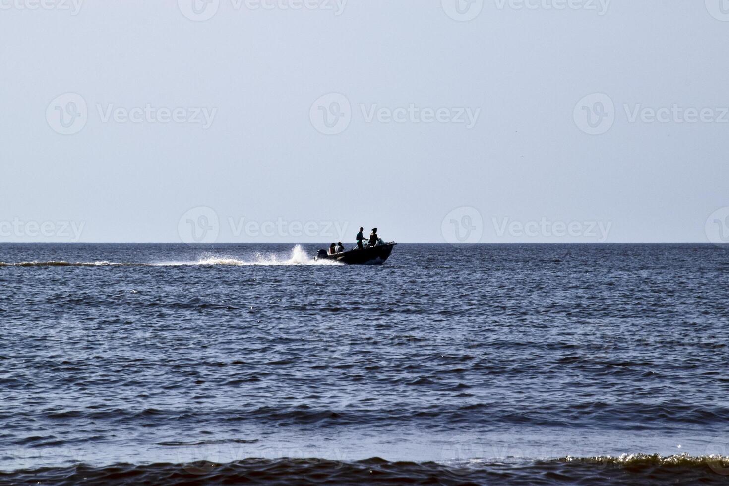 The boat rushes by the sea. In the boat people. Seascape in the evening. Silhouette of a motor boat and people in it against the background of the sea distance photo