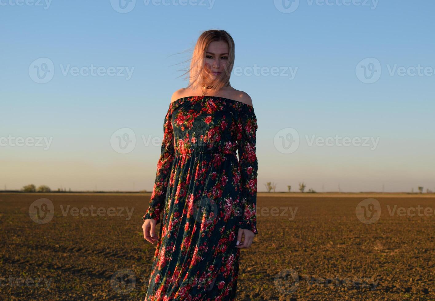 Woman in a plowed field in a red-black dress on a sunset background. photo