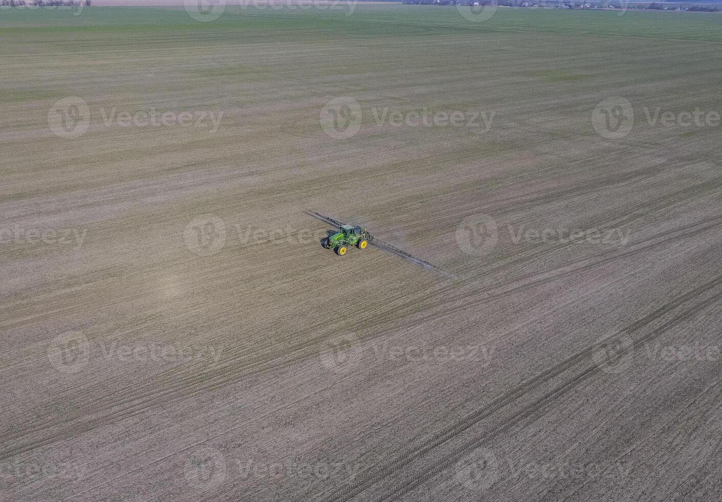 Tractor with hinged system of spraying pesticides. Fertilizing with a tractor, in the form of an aerosol, on the field of winter wheat. photo