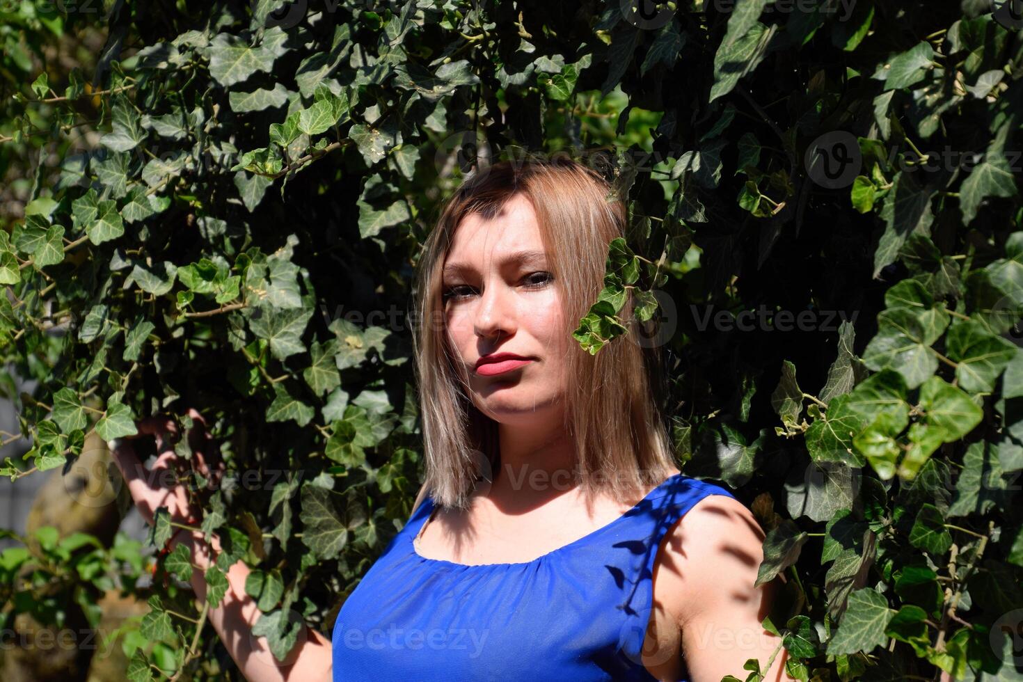 retrato de un niña en un azul vestir en antecedentes de verde cenador de hiedra. foto