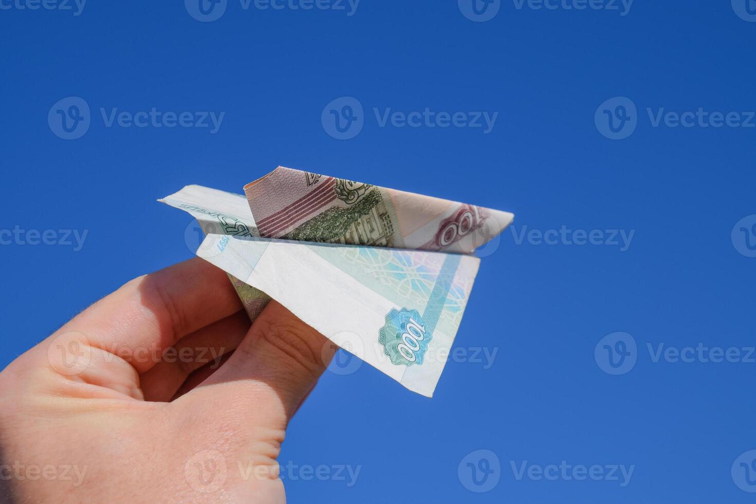Denominations of Russian money, folded in the airplane against the blue sky in hand photo