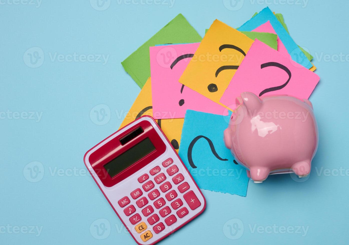 Ceramic piggy bank and stickers with drawn question marks on a blue background, top view photo