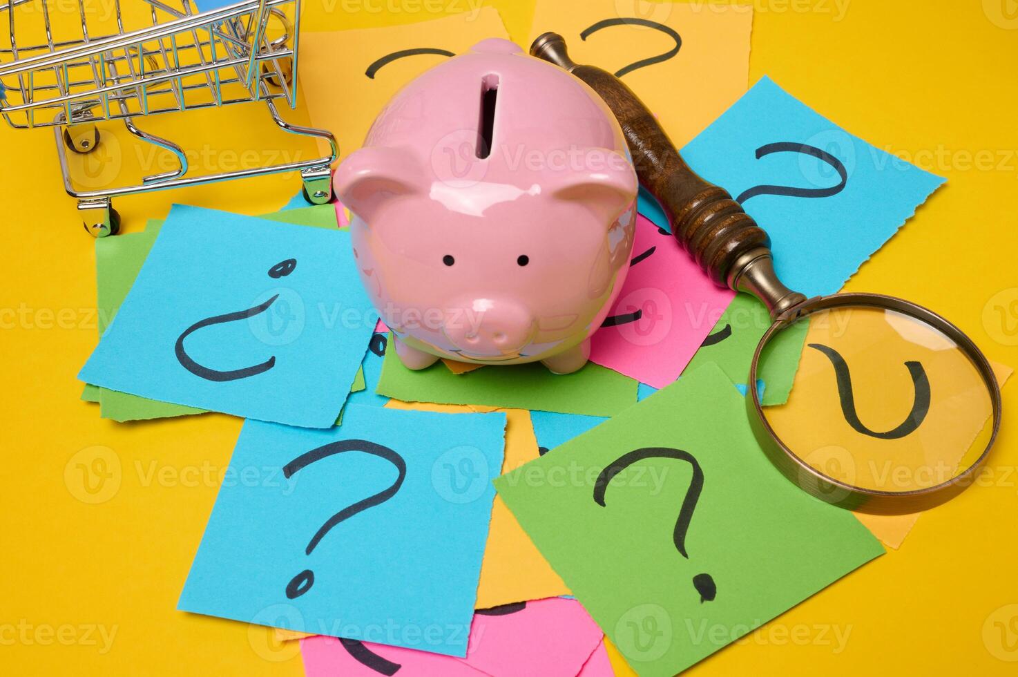 Ceramic piggy bank and stickers with drawn question marks on a yellow background, top view photo