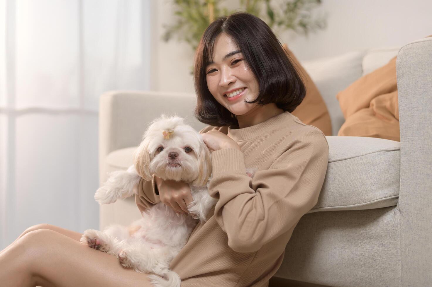 Happy young asian woman cuddling and spending time with cute dog in living room. photo