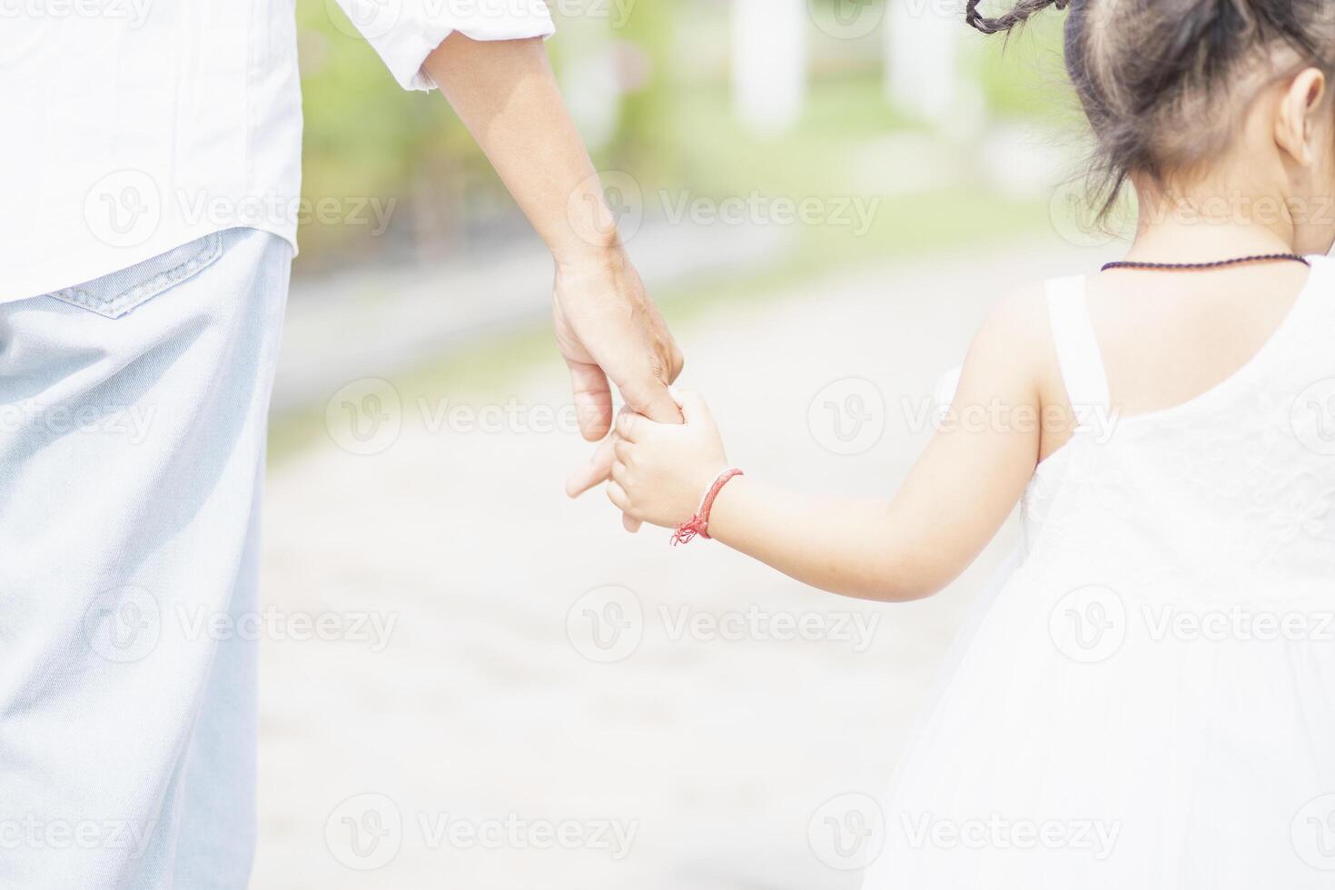 Little girl with her father on nature background A back view of the Father in Heaven concept. Father holds daughter's hand as she walks. photo