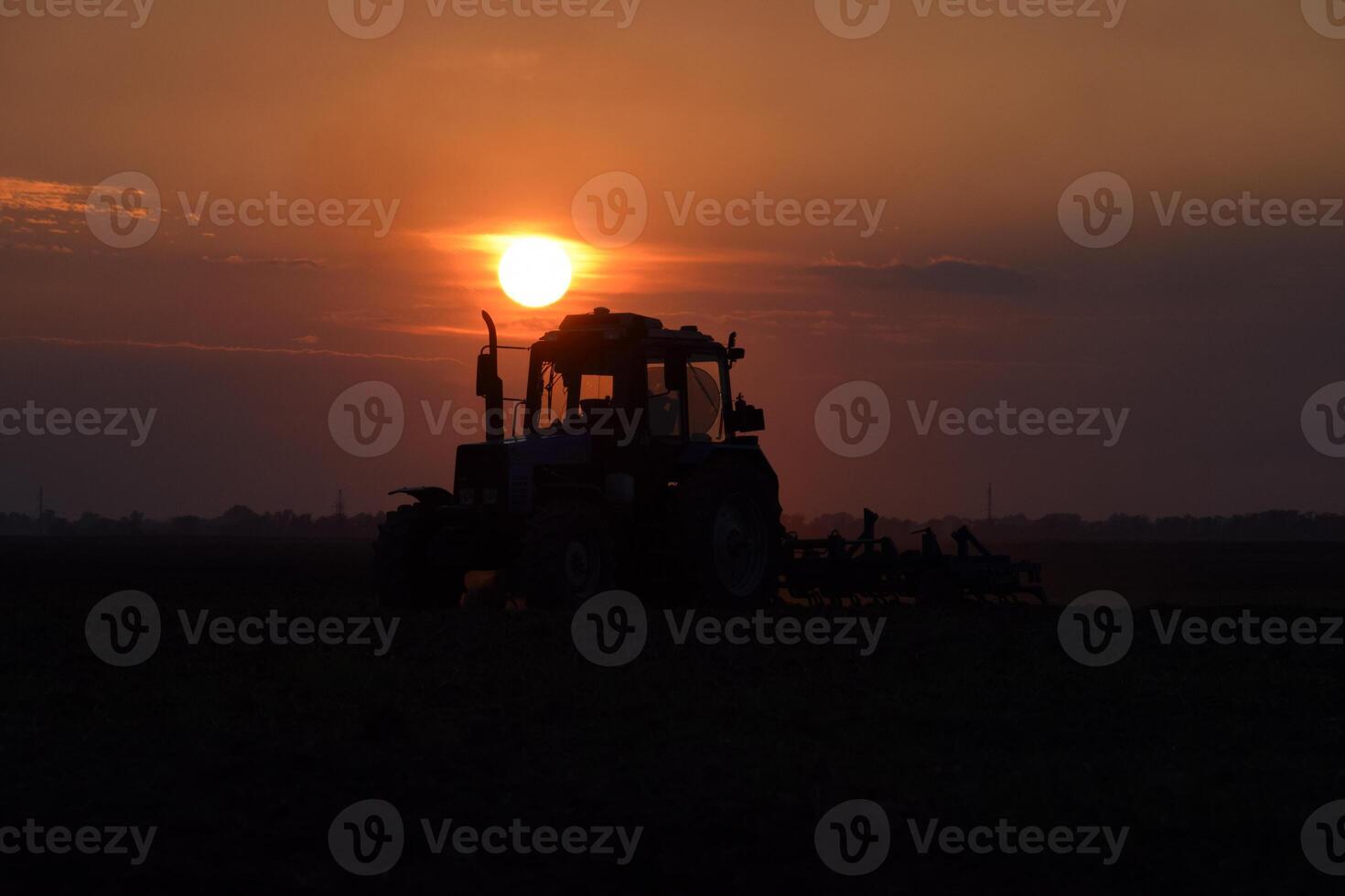 Tractor plowing plow the field on a background sunset. tractor silhouette on sunset background photo