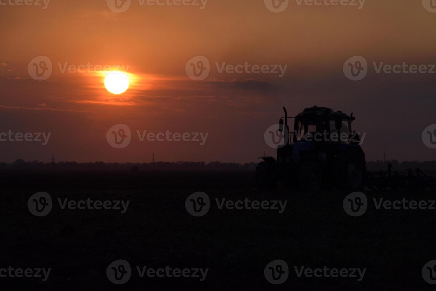 Tractor plowing plow the field on a background sunset. tractor silhouette on sunset background photo
