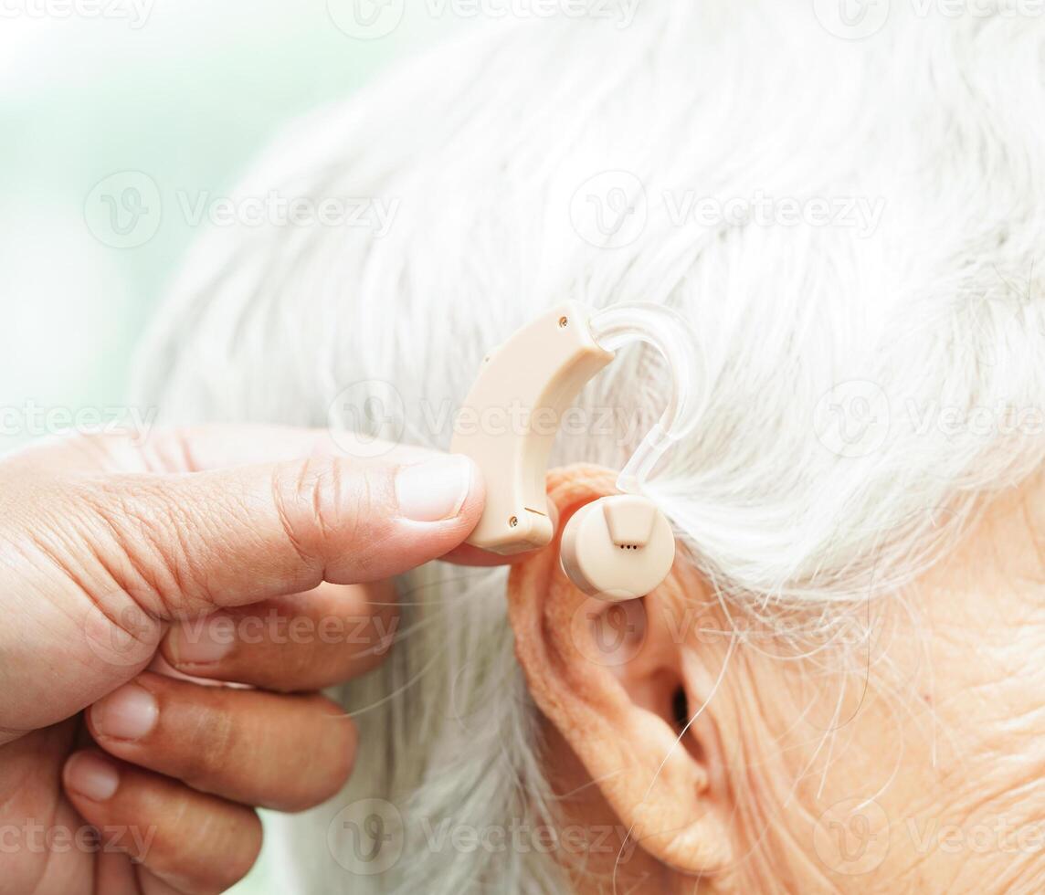 Doctor install hearing aid on senior patient ear to reduce hearing loss problem. photo