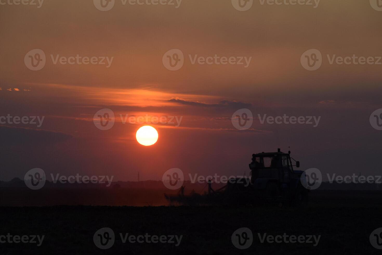 Tractor plowing plow the field on a background sunset. tractor silhouette on sunset background photo