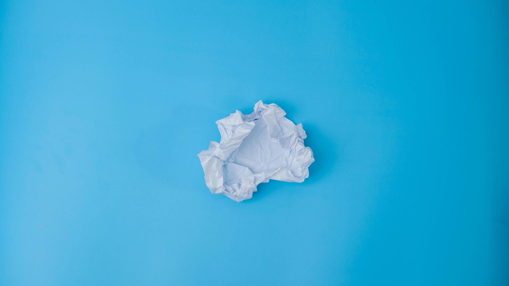 A paper ball is spread out into a blank sheet on blue background. Crumpled blank white paper with copy space for text or advertising space. photo