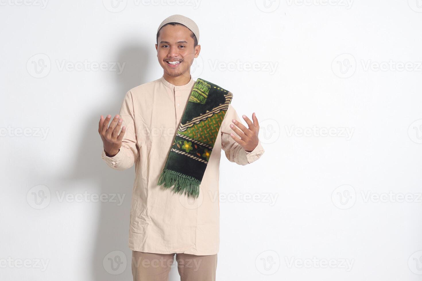 Portrait of attractive Asian muslim man in koko shirt with skullcap inviting and welcoming someone to come in. Isolated image on white background photo