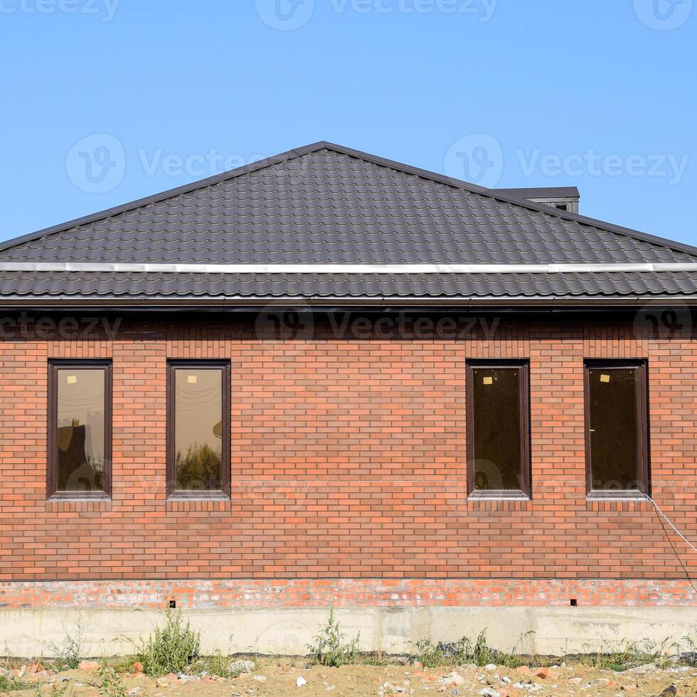 The house with plastic windows and a roof of corrugated sheet. Brown roof and brown brick photo