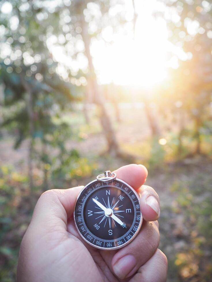 Close up of compass in woman hand with forest in the sunset time as background. The concept of world tourism day, Searching the right directions and Travel photo