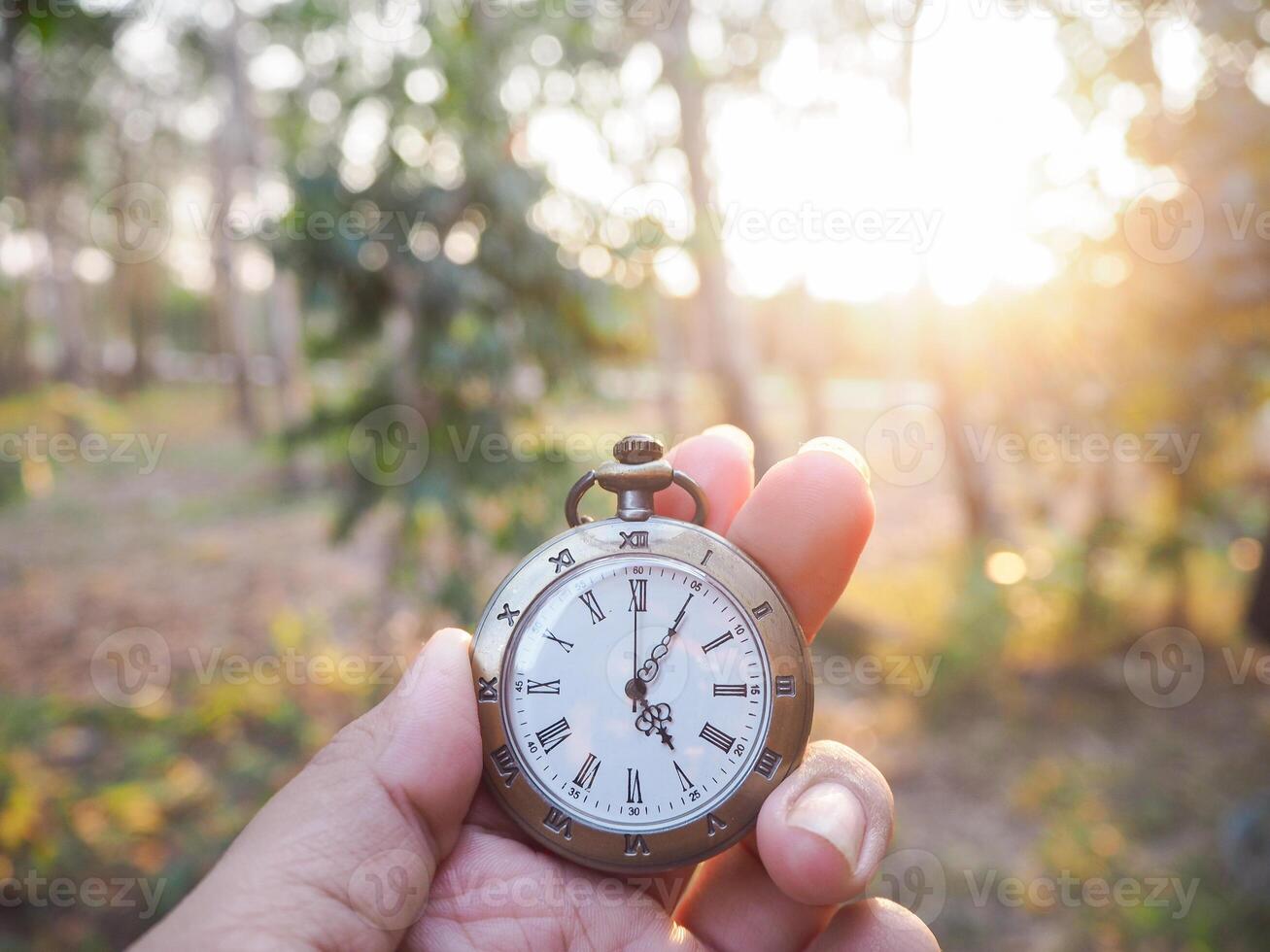 cerca arriba de Clásico bolsillo reloj en mujer mano con bosque en el puesta de sol hora como antecedentes. foto