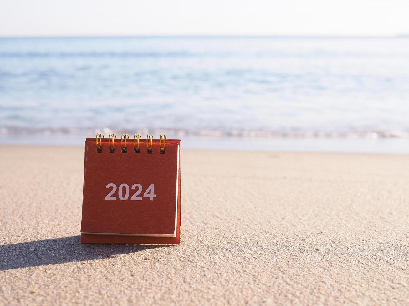 Close up 2024 desk calendar on the beach in the sunset time. Resolution, Goal, Action, Planning, and manage to success business. photo