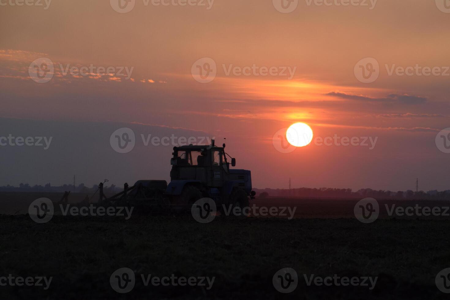 Tractor plowing plow the field on a background sunset. tractor silhouette on sunset background photo