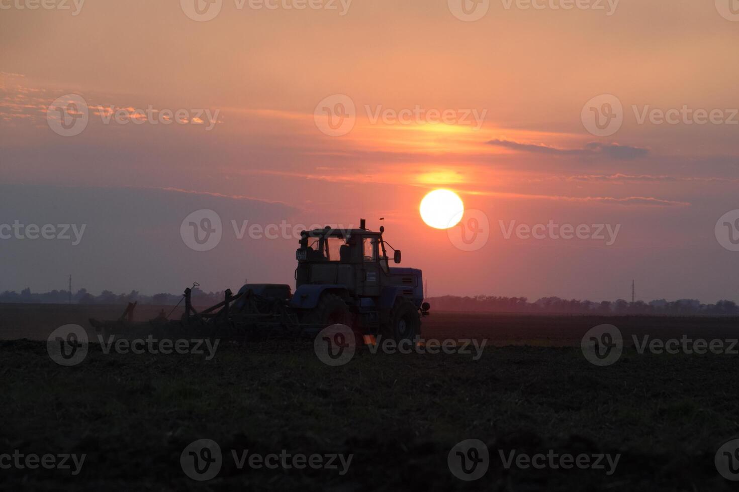 Tractor plowing plow the field on a background sunset. tractor silhouette on sunset background photo