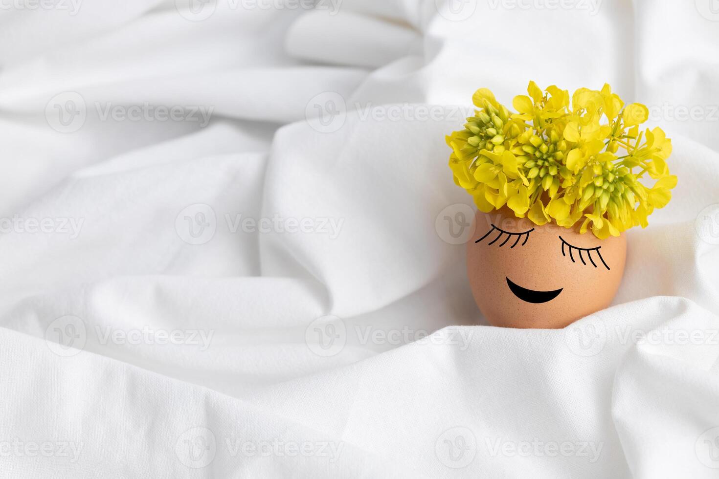 Easter egg with cute face and wreath of yellow flowers on white fabric background photo